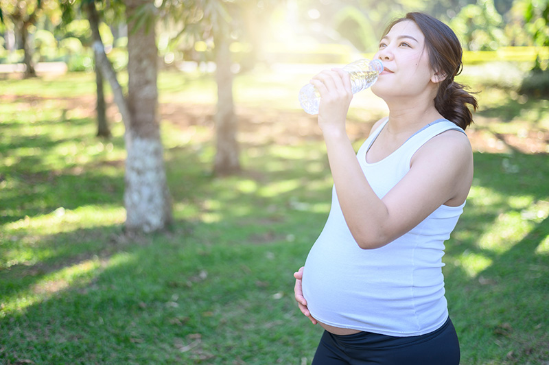 a pregnant person outside in a park drinking from a bottle of water