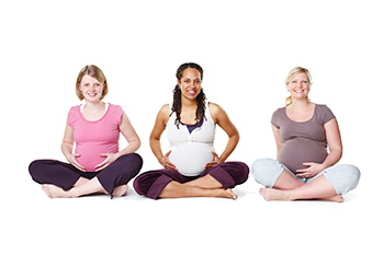 three smiling pregnant women in a row, all seated cross-legged
